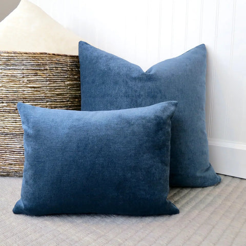 Soft blue velvet pillows, one square, one lumbar, propped against a wall for display.